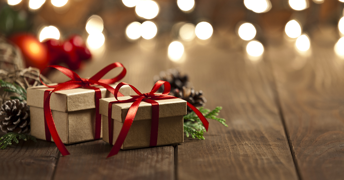 Horizontal view of two brown Christmas gift boxes shot on rustic wood table. The boxes are tied up with a red ribbon and Christmas lights are out of focus behind the group of boxes. The two boxes are grouped at the left side of the frame leaving a useful copy space ready for text and/or logo at the right. Predominant colors are brown and red. DSRL studio photo taken with Canon EOS 5D Mk II and Canon EF 70-200mm f/2.8L IS II USM Telephoto Zoom Lens